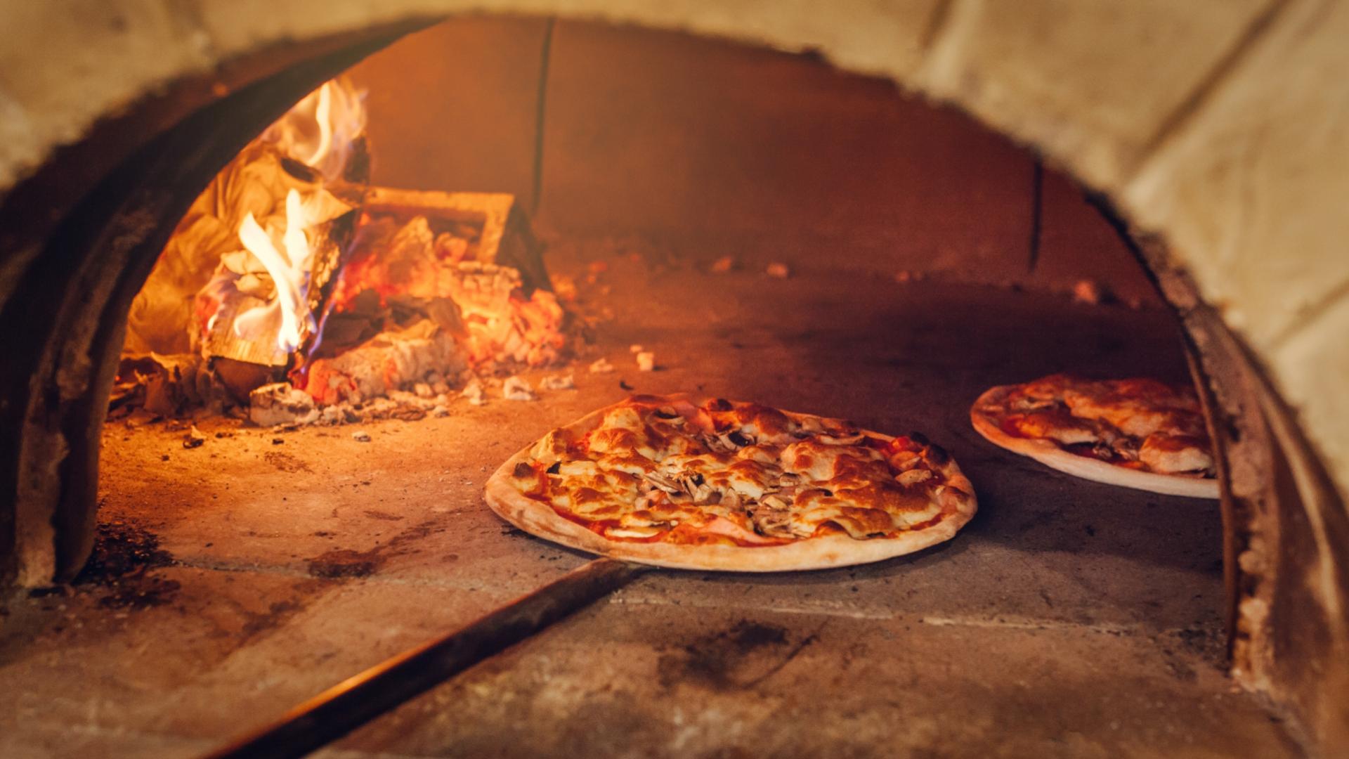 Pizze che cuociono in forno a legna con fiamma viva.