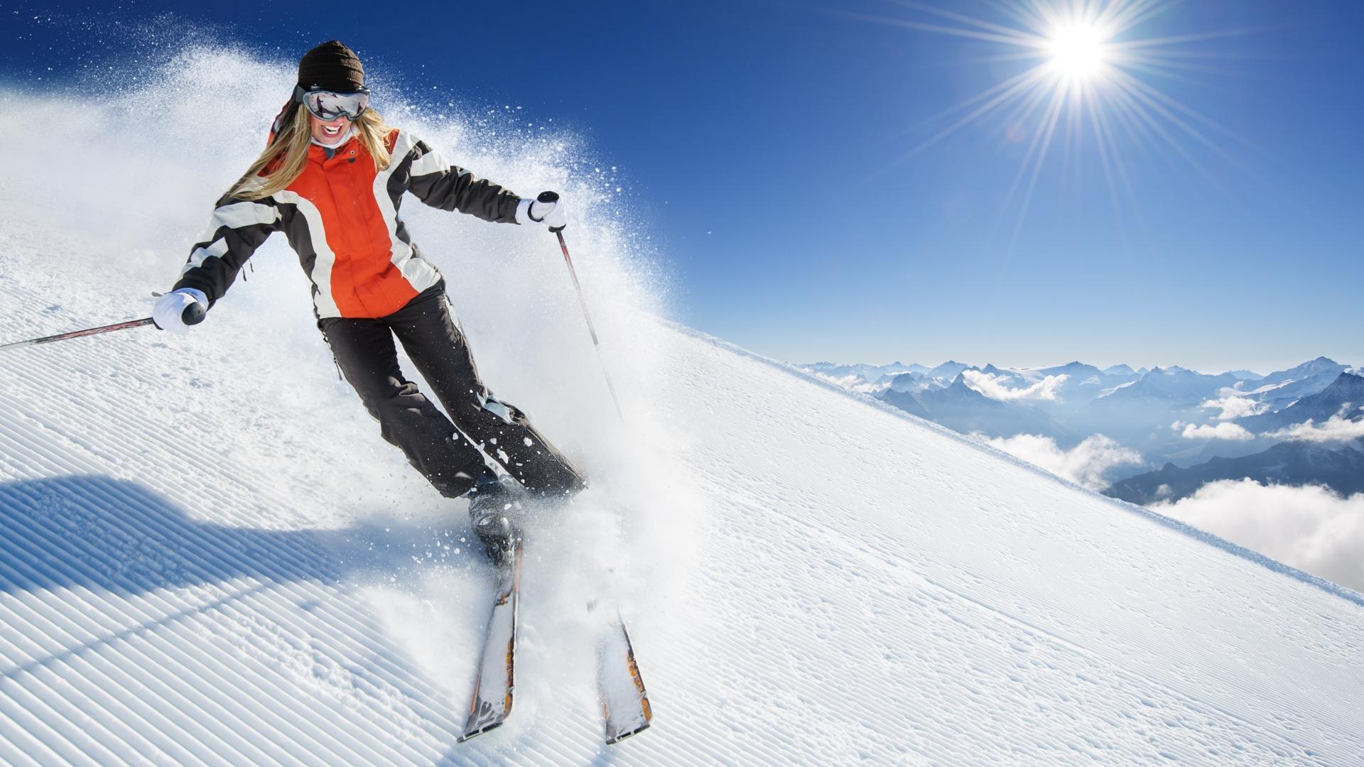 Sciatore in azione su una pista innevata con cielo limpido e sole splendente.