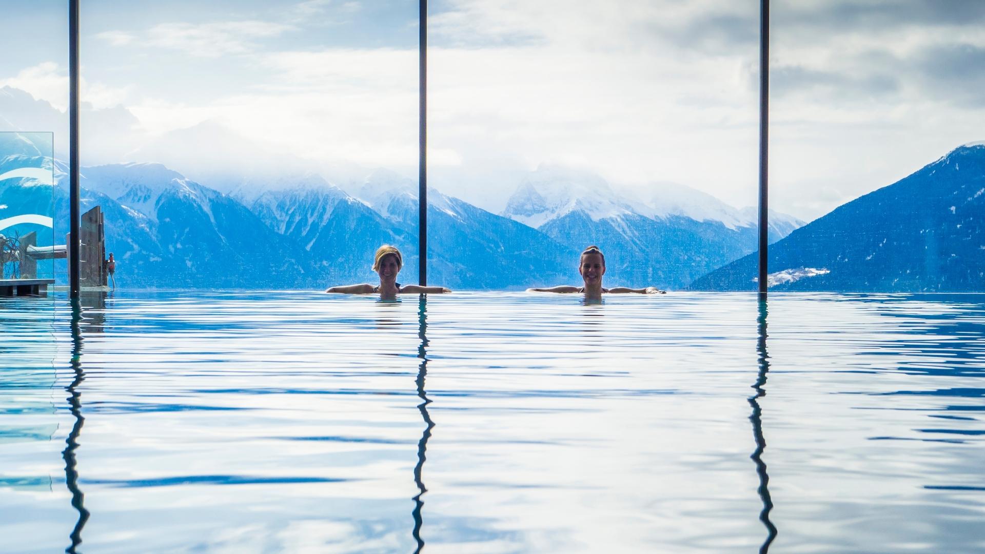 Due persone in piscina con vista sulle montagne innevate.