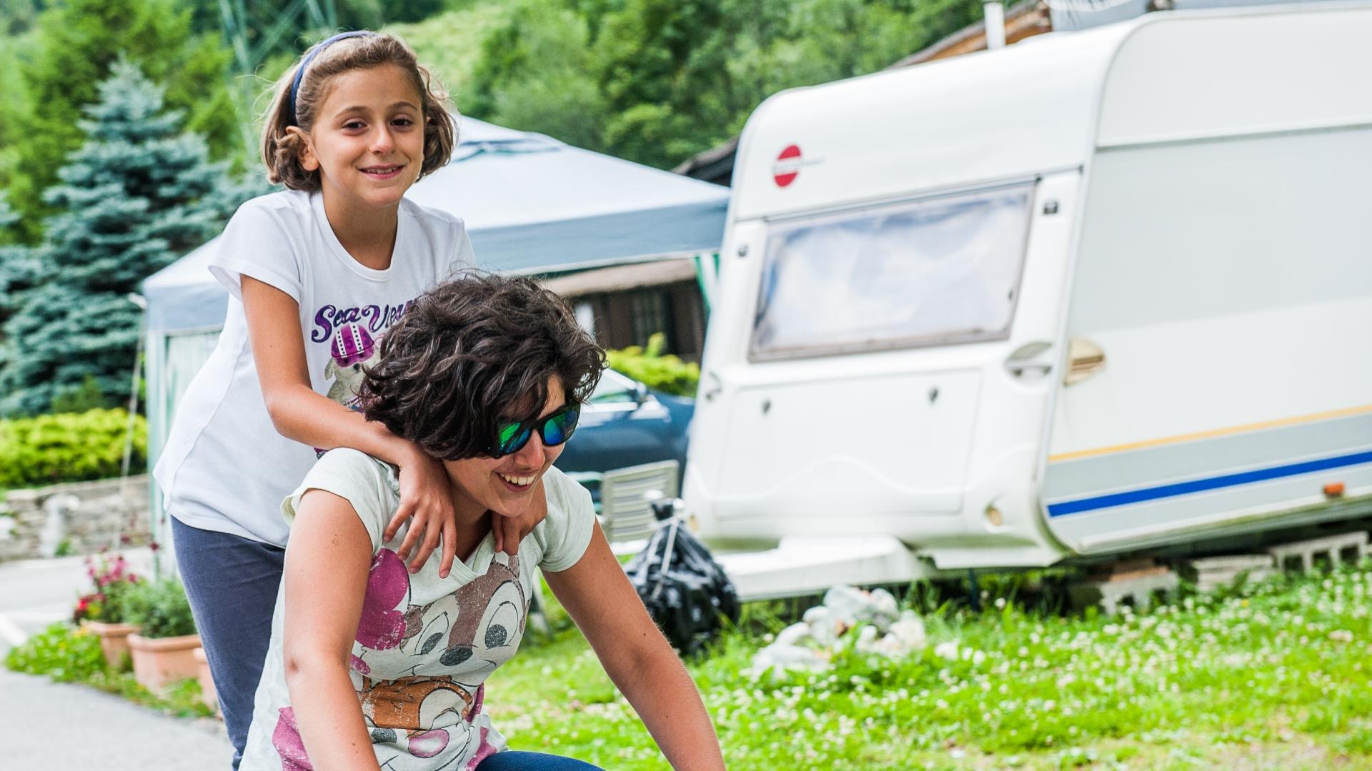 Une fille monte sur le dos d'une femme, près d'une caravane.