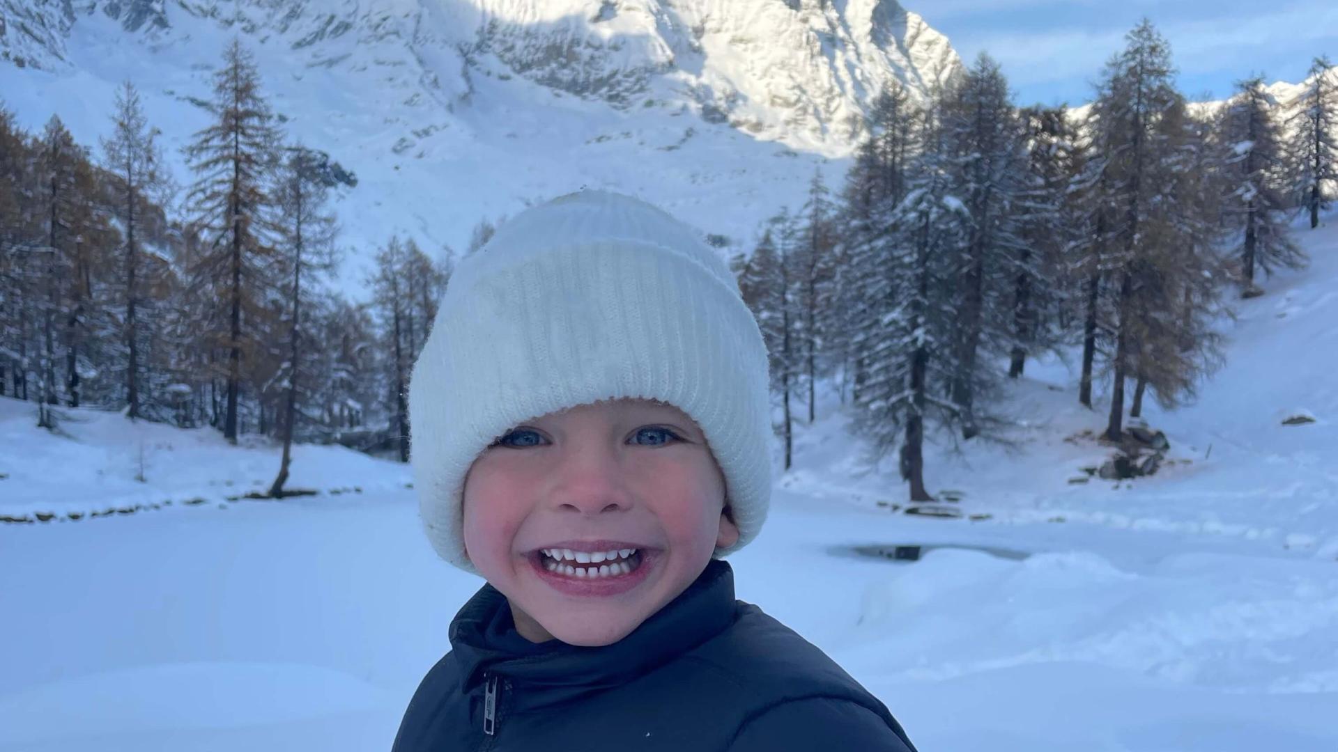 Bambino sorridente sulla neve con montagna sullo sfondo.