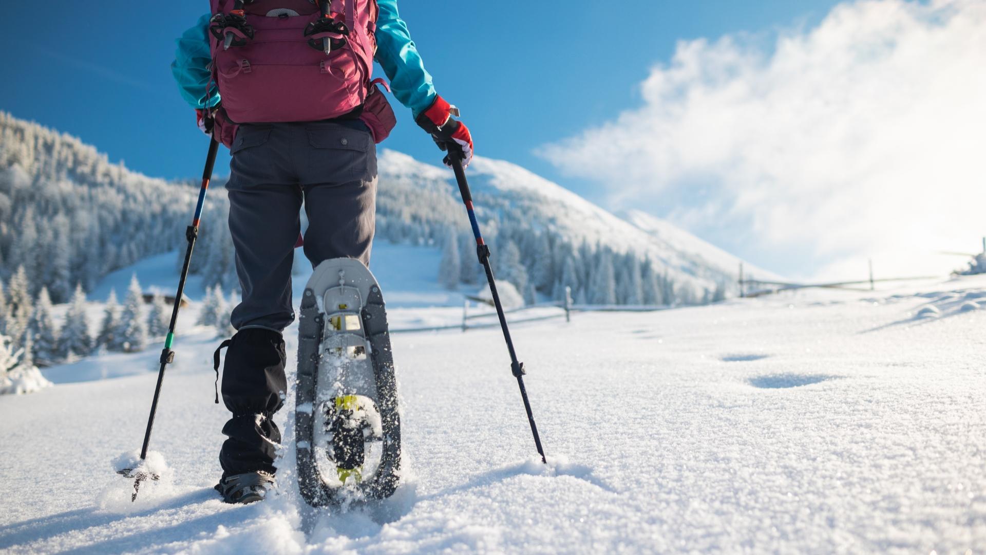 Persona con racchette da neve cammina su un sentiero innevato in montagna.