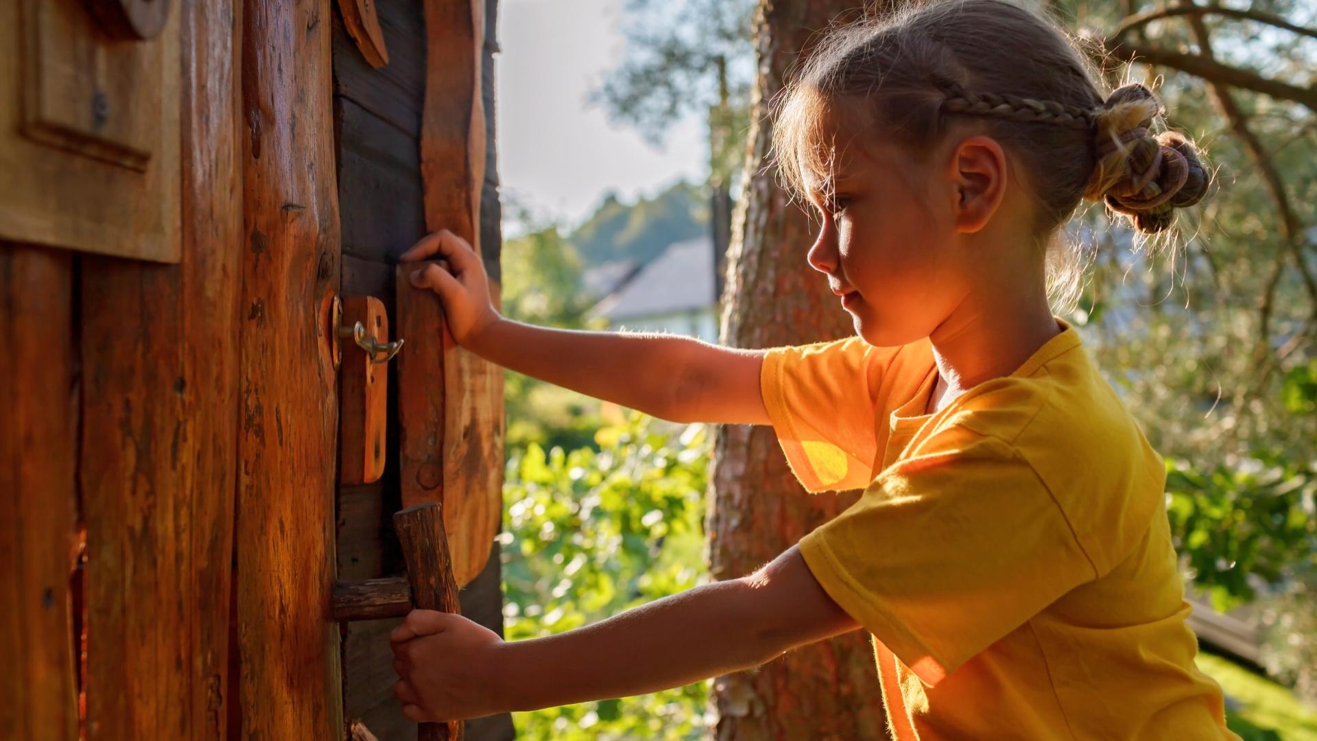 Bambina apre una porta di legno in una casa sull'albero.