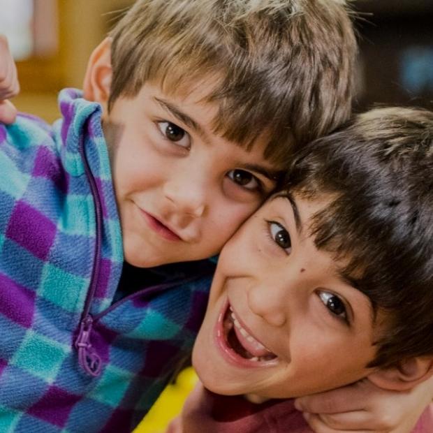 Due bambini sorridenti si abbracciano, uno con una felpa a scacchi colorati.