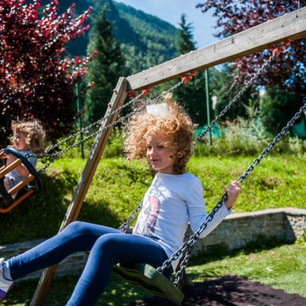 Bambini che giocano sull'altalena in un parco con un adulto che li osserva.