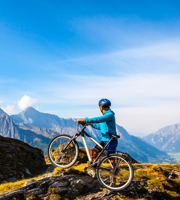 Ciclista in montagna con bici, panorama mozzafiato e cielo blu.