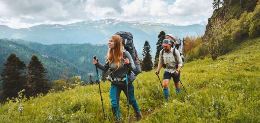 Due escursionisti camminano su un sentiero di montagna con zaini e bastoni da trekking.