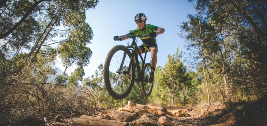 Ciclista salta su una mountain bike in un sentiero boschivo.