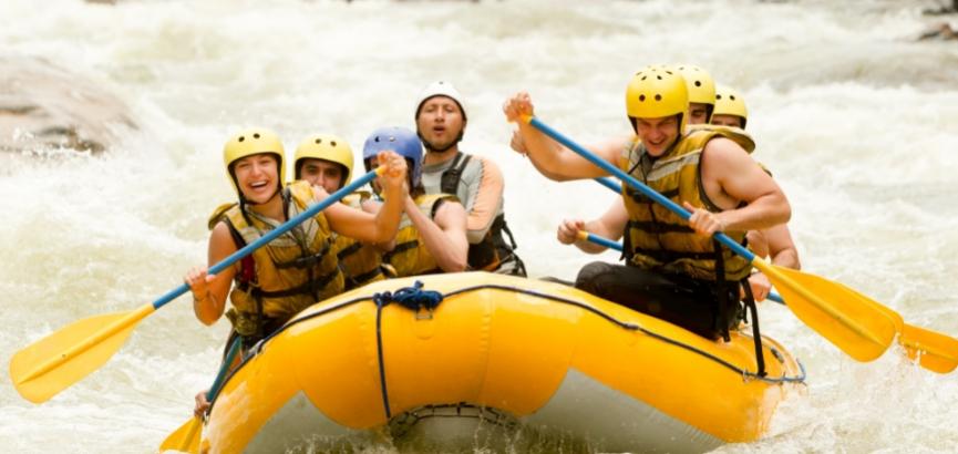 Gruppo di persone che fa rafting in un fiume con caschi e pagaie.