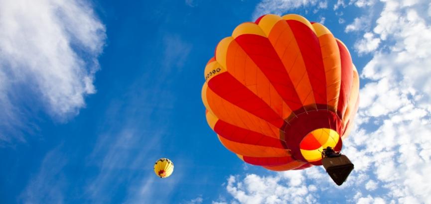 Due mongolfiere colorate volano nel cielo azzurro con nuvole bianche.