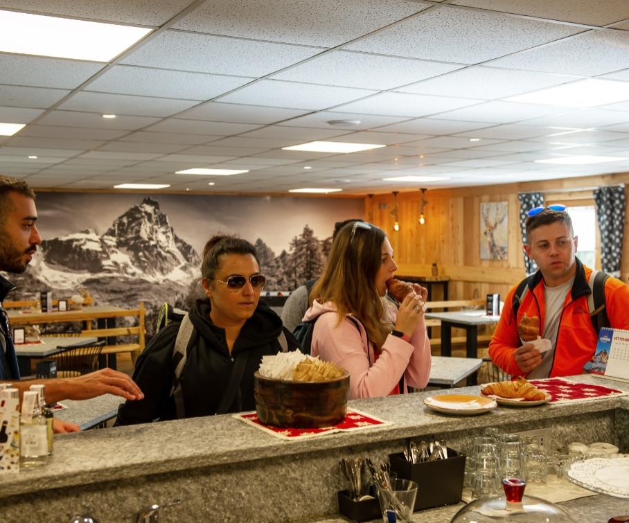 Persone al bar, mangiando cornetti e bevendo caffè in un ambiente montano.