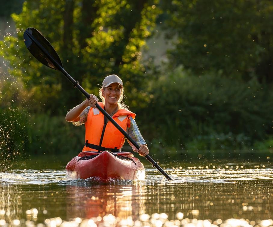 Donna in kayak con giubbotto di salvataggio su un fiume al tramonto.