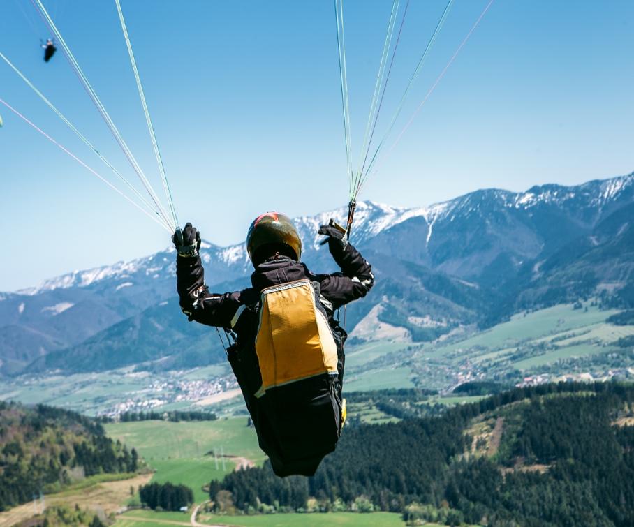 Parapendio sopra una valle verde con montagne innevate sullo sfondo.