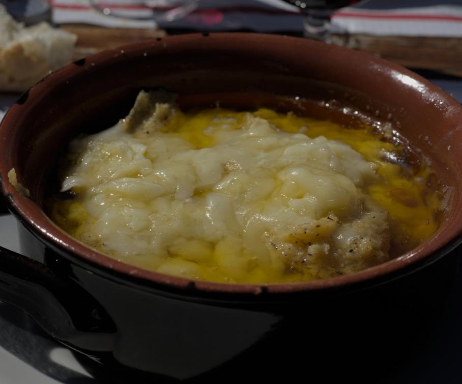 Zuppa di cipolle gratinata con formaggio fuso in una ciotola di terracotta.