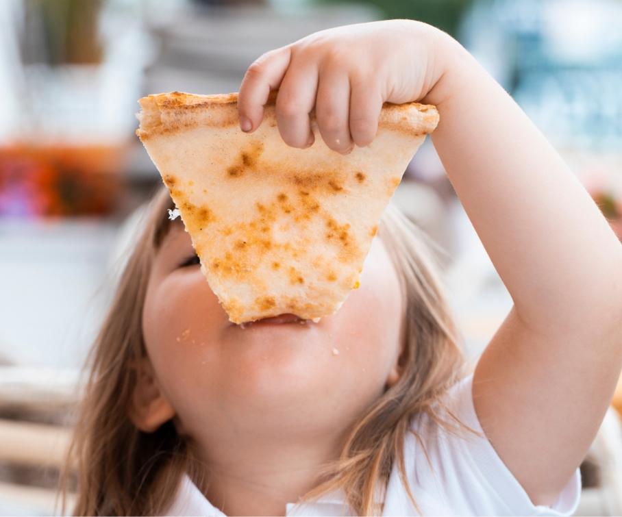 Bambina che mangia una fetta di pizza con entusiasmo.