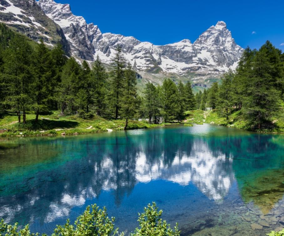 Lago alpino con acque cristalline, circondato da foreste e montagne innevate.