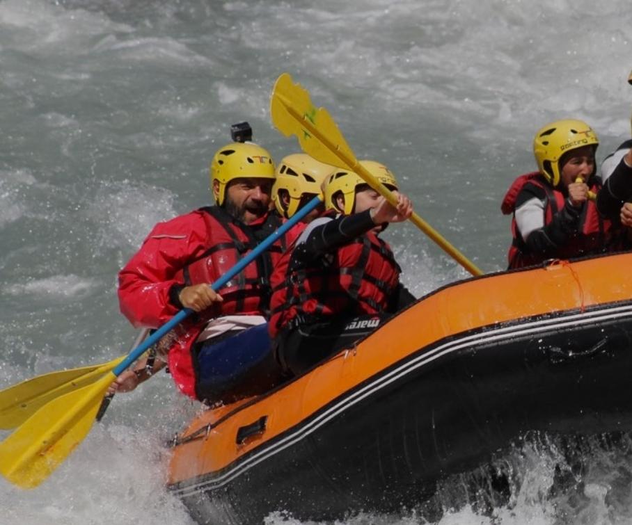 Gruppo di persone fa rafting su un fiume con caschi e giubbotti di salvataggio.