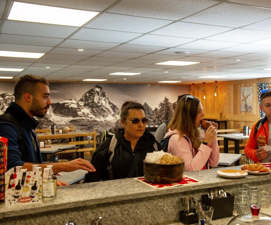 Persone fanno colazione in un bar di montagna con vista sulle Alpi.