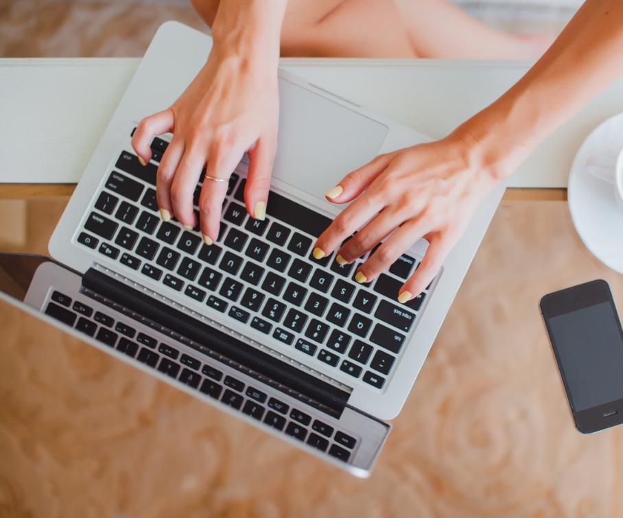 Mani che digitano su un laptop, con uno smartphone e una tazza di caffè accanto.