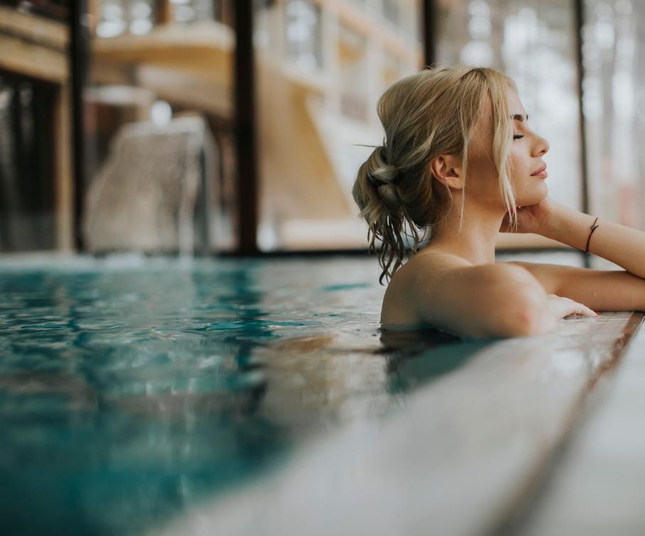 Donna rilassata in piscina coperta, con acqua limpida e sfondo sfocato.