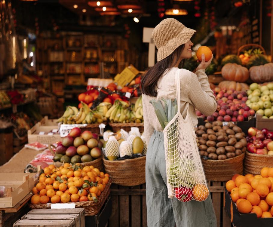 Donna con cappello compra frutta in un mercato all'aperto.