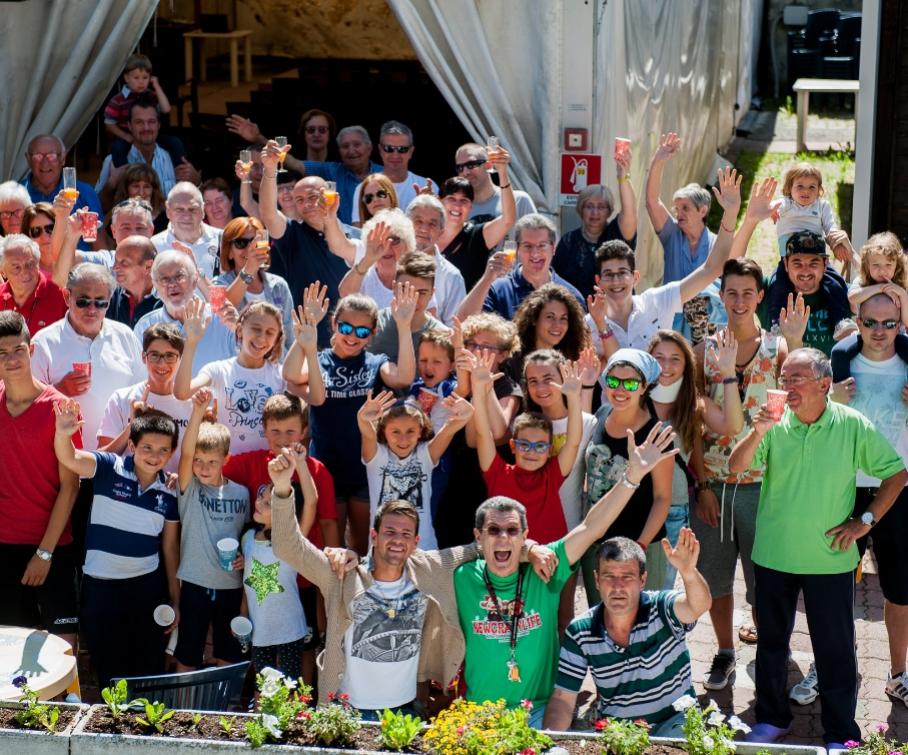 Gruppo di persone sorridenti che salutano e brindano all'aperto.