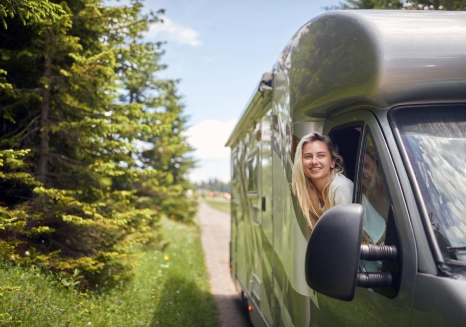 Donna sorridente in camper verde, immersa nella natura.