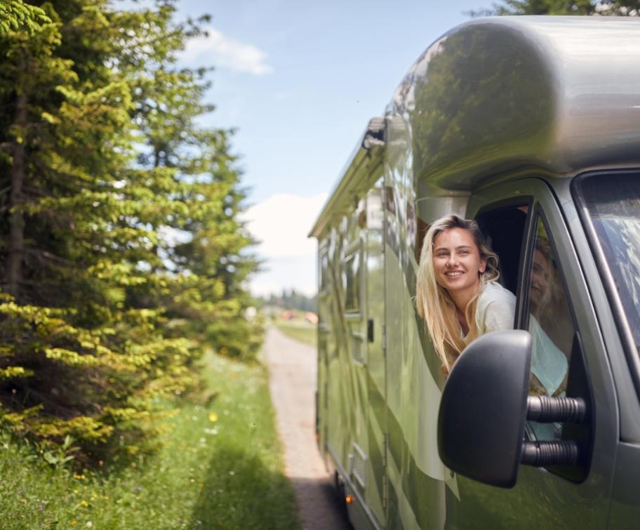 Donna sorridente in camper verde, immersa nella natura.