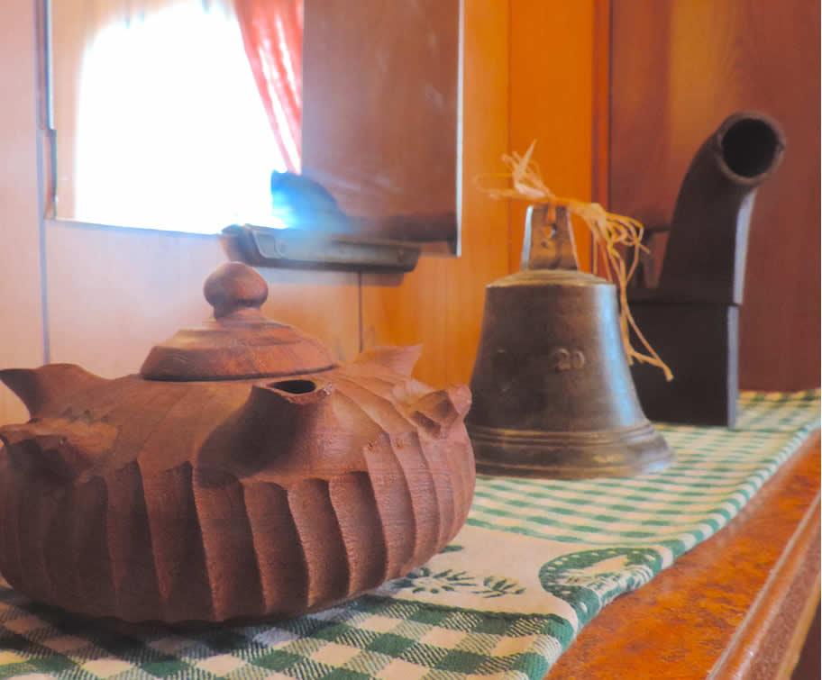 Teiera in legno, campana e oggetto antico su tovaglia a quadri verdi.