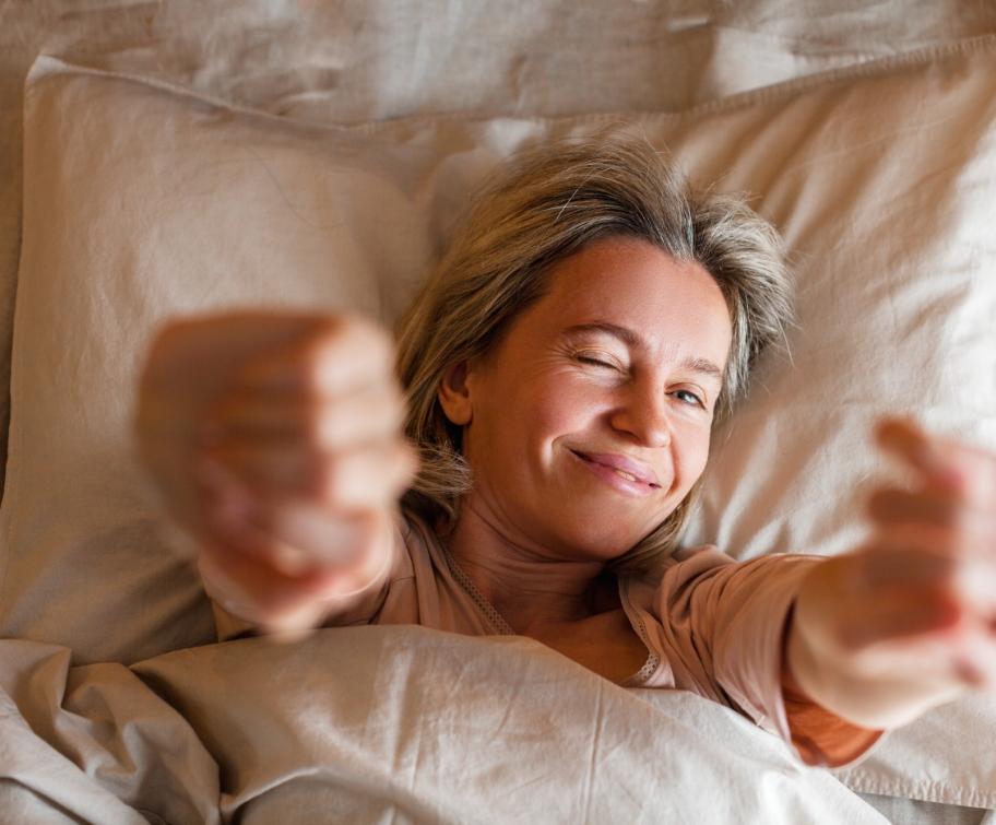 Donna sorridente che si stira nel letto, pronta per iniziare la giornata.