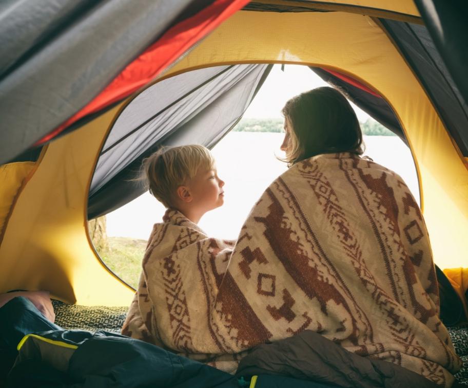 Due persone avvolte in una coperta all'interno di una tenda da campeggio.