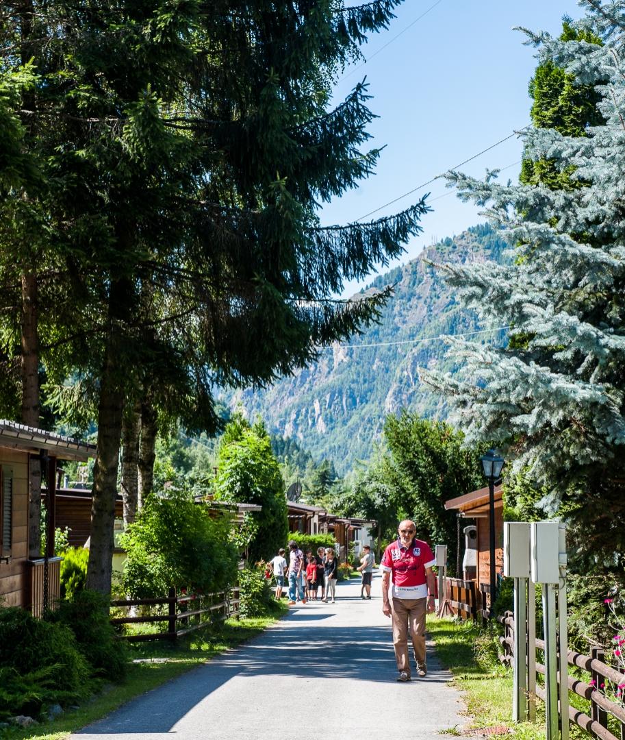 Un uomo cammina in un villaggio montano con case di legno e alberi.